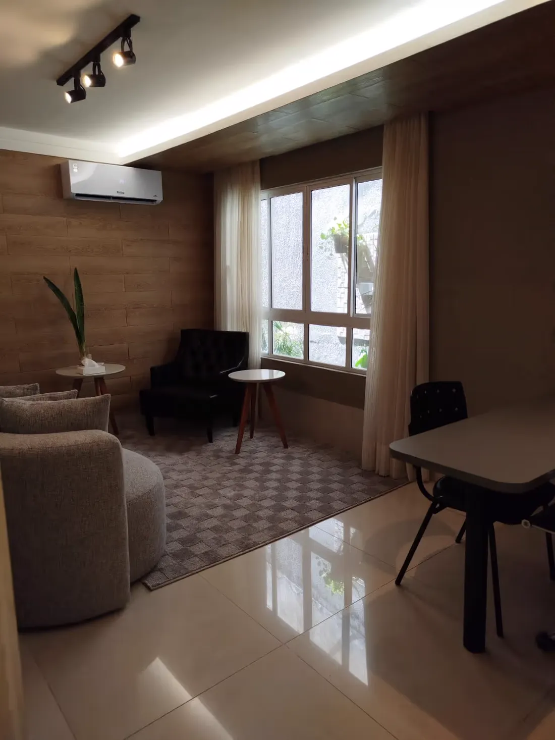 Sala com poltronas, tapete, mesa de apoio e janela ampla