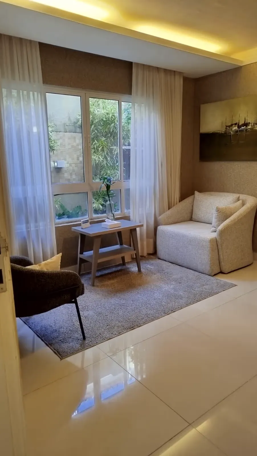 Sala com cortinas claras, poltronas e mesa de centro