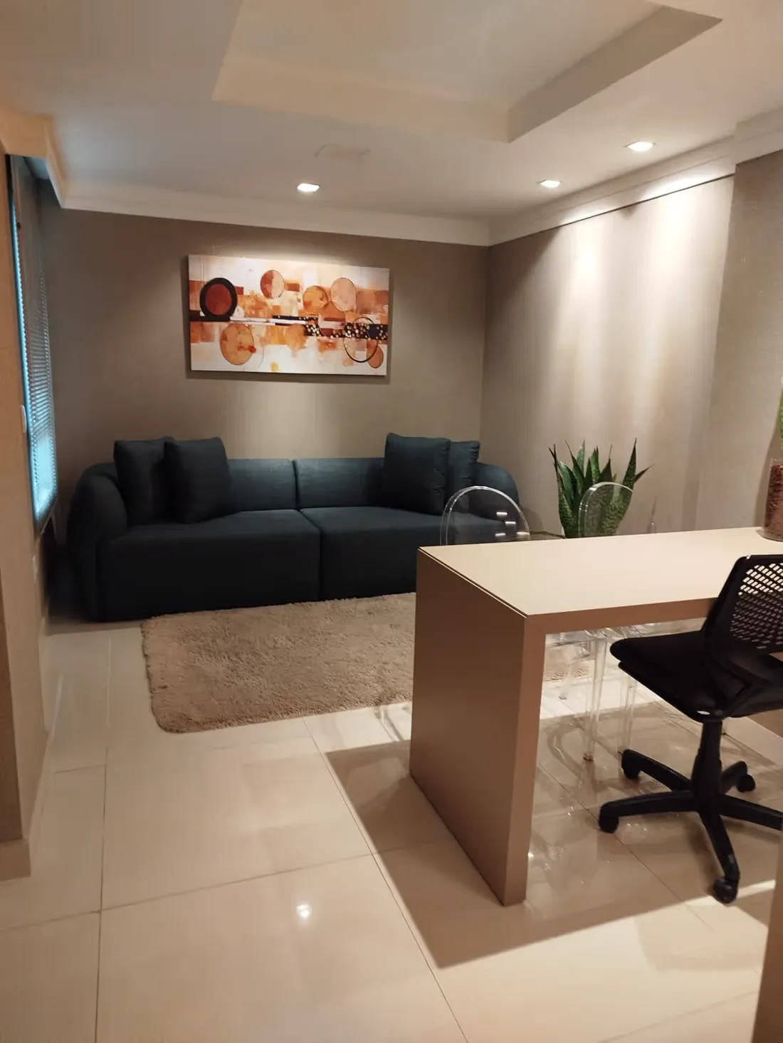 Sala da psiquiatria com sofá escuro, mesa de trabalho e quadro abstrato